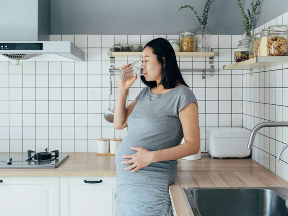 Pregnant woman drinking glass of water in kitchen at home