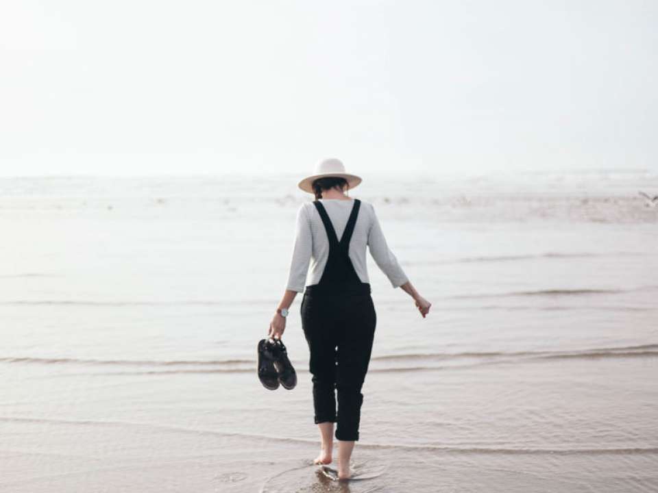 Woman in hat walks in shallow ocean water