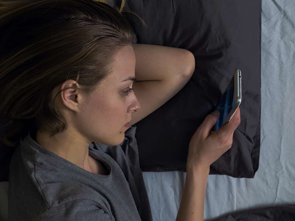a young woman lying in bed looking at her phone