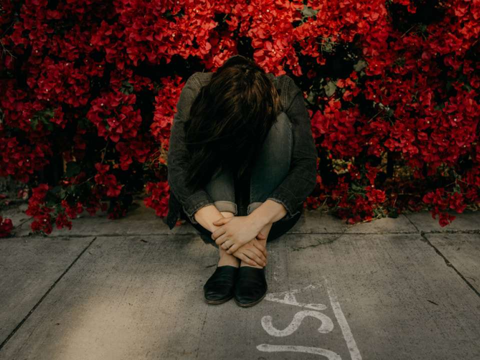 Woman with head down sitting amidst red flowers