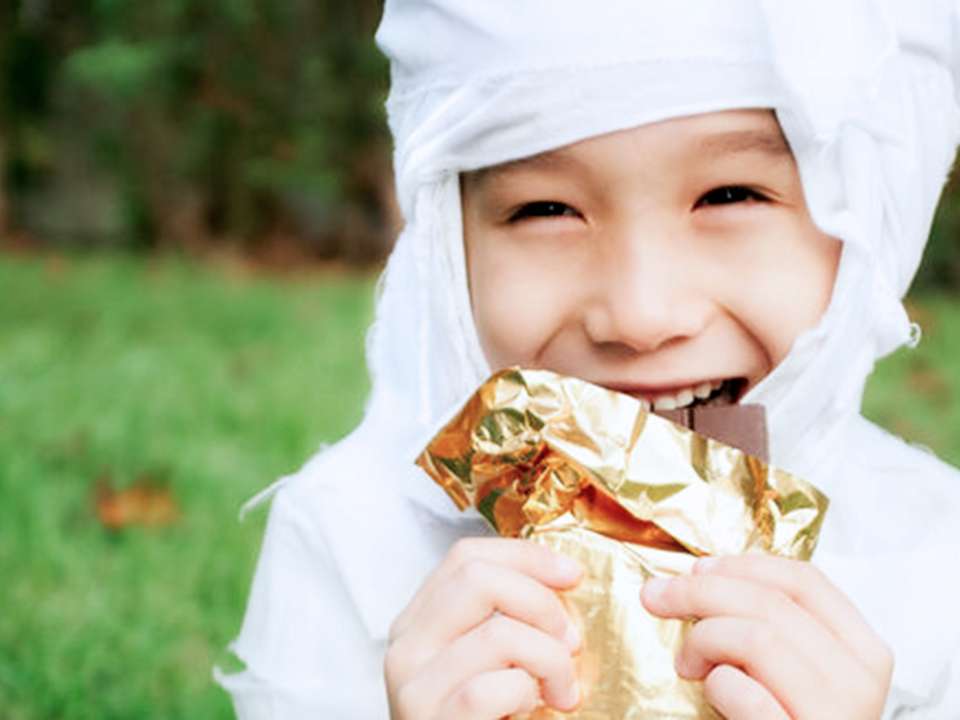 A young boy dressed as a mummy eats a bar of chocolate.