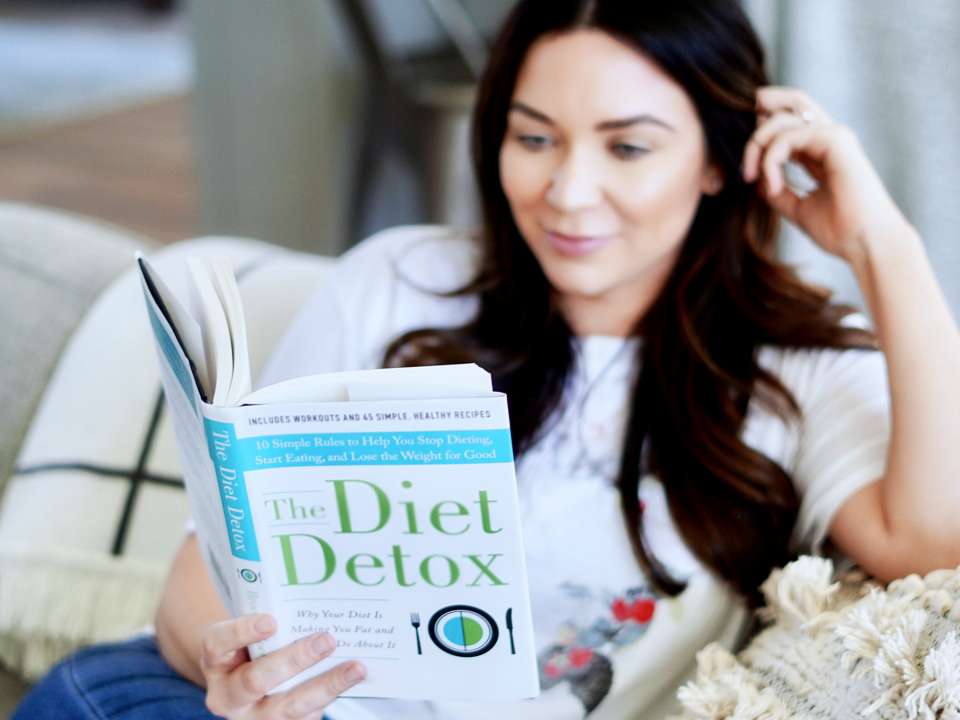 A woman sitting on the couch reading a diet book.