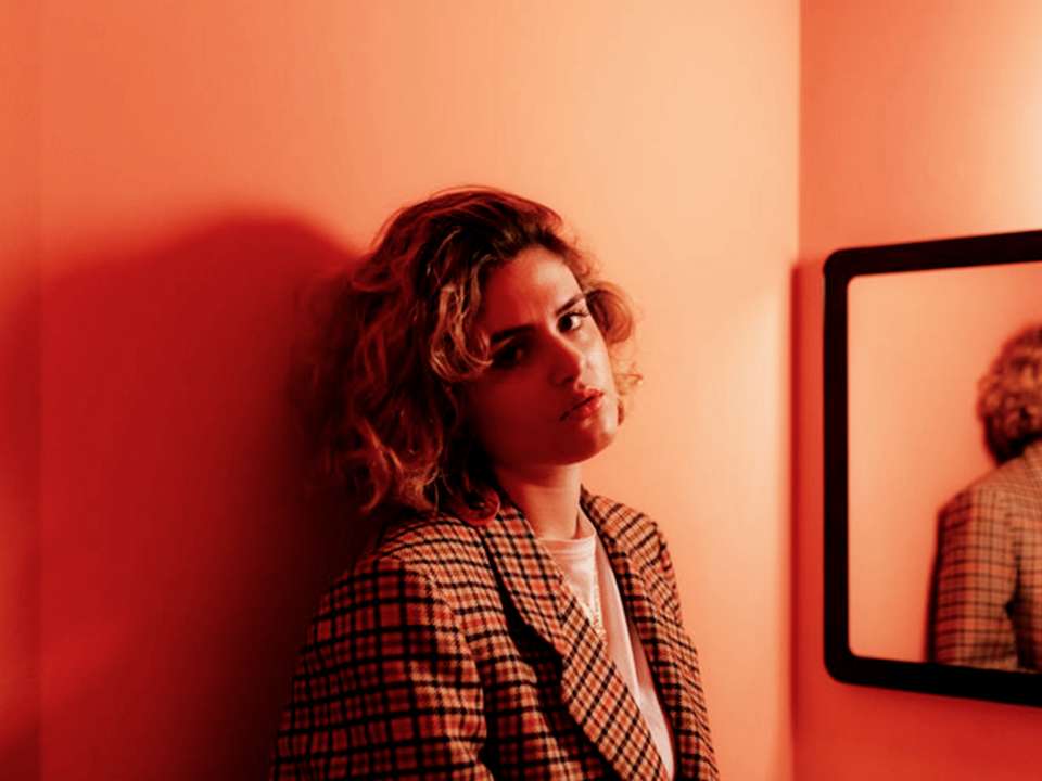 A woman leaning against the wall in a red room looking irritated.