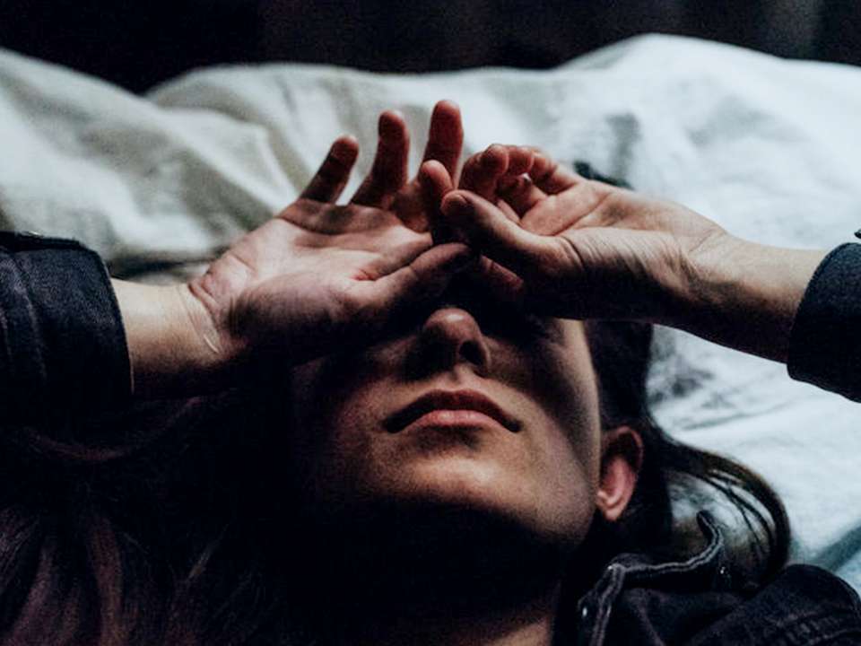 A woman with a headache lies down on a bed.