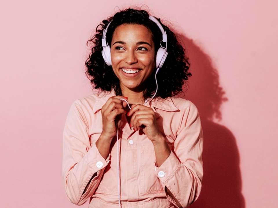 Woman listening to headphones with pink backdrop