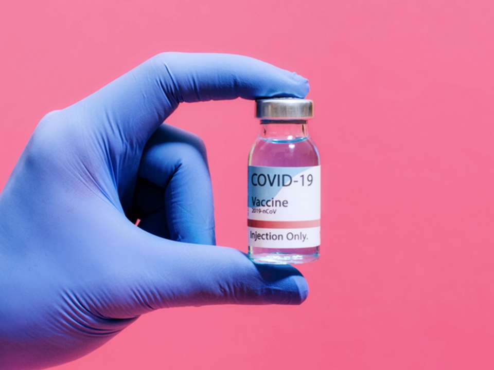 gloved hand holding COVID vaccine vial