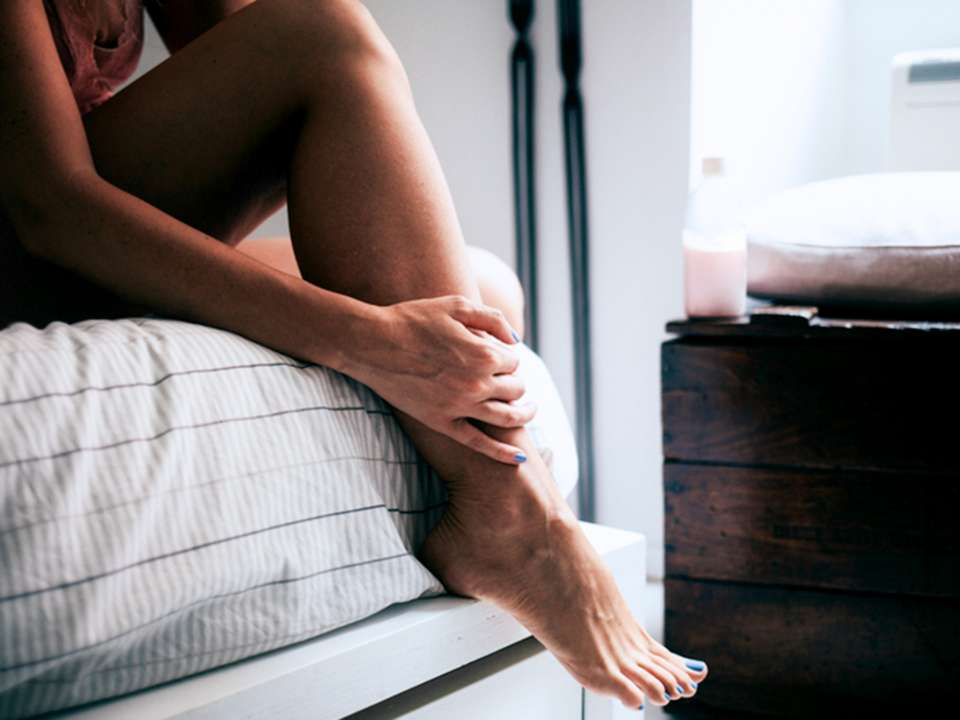 woman sitting on side of bed holding leg