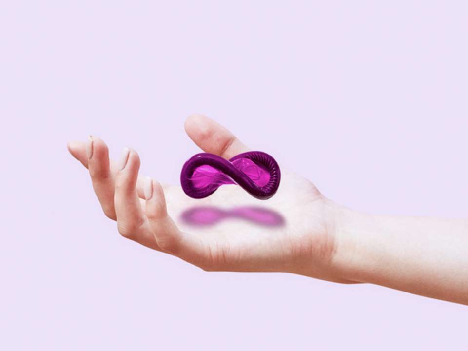A purple condom in the shape of an infinity symbol floats above a woman's outstretched hand.