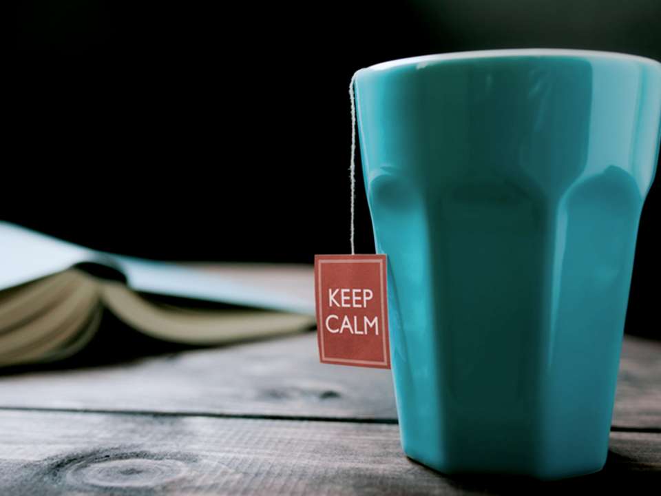 A blue mug on a wooden table with a teabag tag hanging out of it that says Keep Calm.