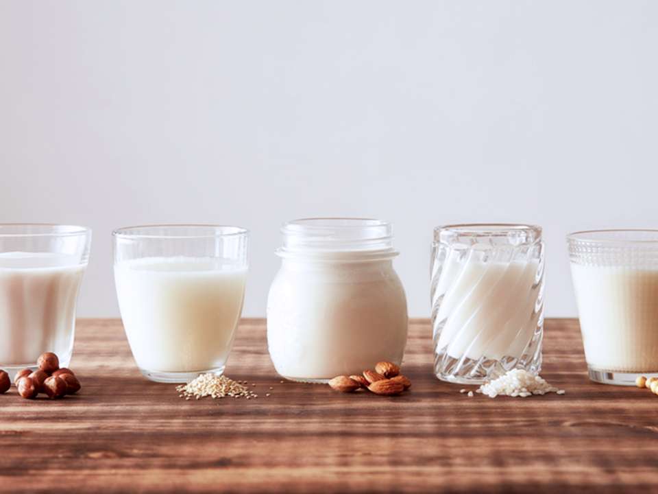 A lineup of non-dairy milk alternatives in glasses.