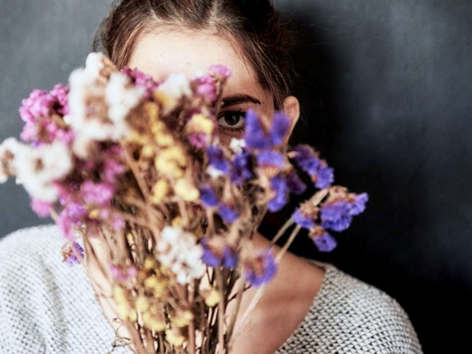 A woman holds dried flowers up to partially cover her face.