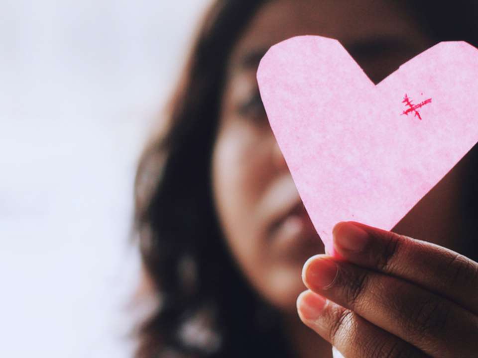 A woman holds up a paper cutout of a heart.
