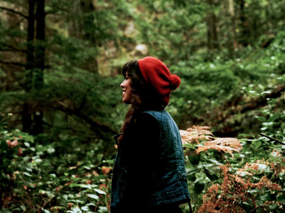 A woman with a red hat stands in a green forest.
