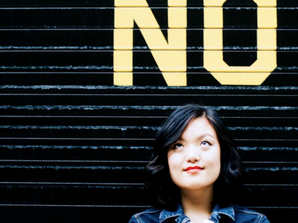 A woman stands under the word 'No' and is looking up at it.