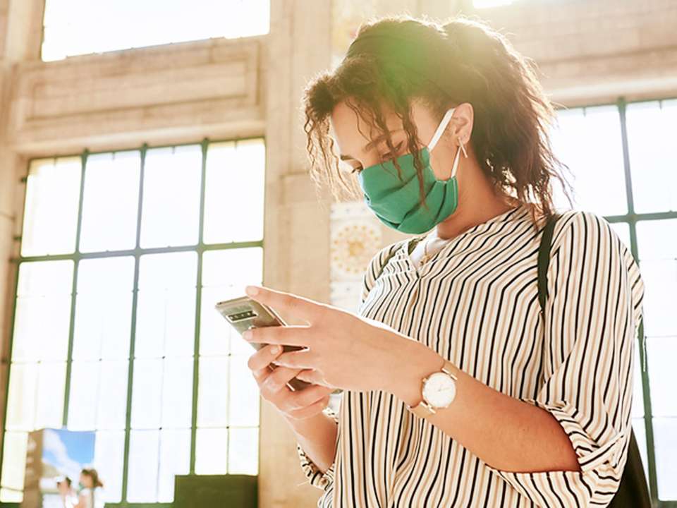 A woman wears a mask out in public while looking at her phone.