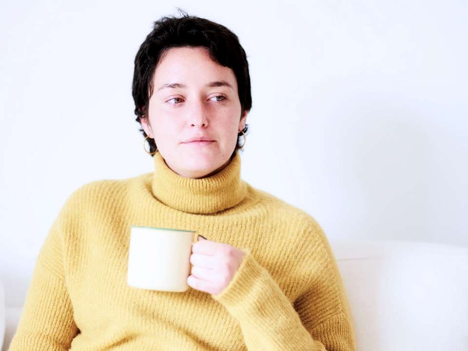 A woman in a yellow sweater looks on thoughtfully.