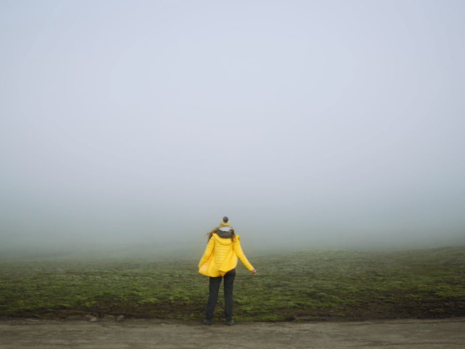 A woman standing in thick fog facing away from the camera