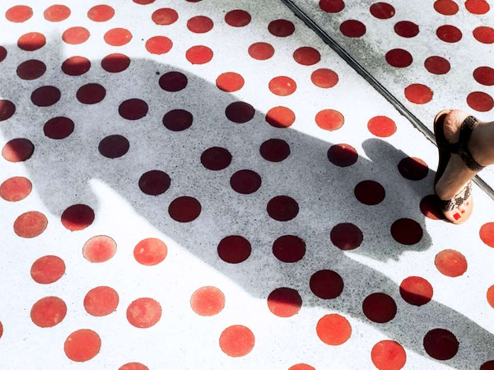 Pavement covered in red dots with a woman walking by.