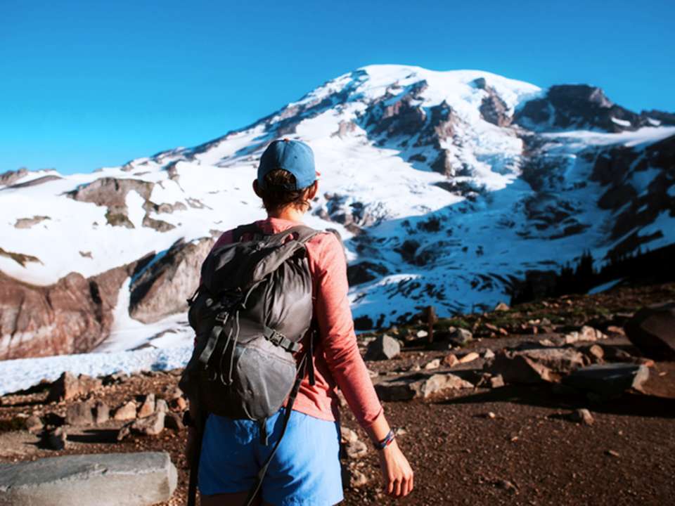 A woman with a hiking backpack stands looking at Mt. Rainier.