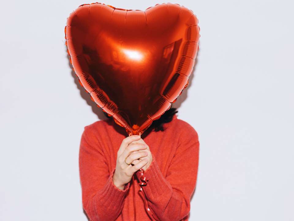 Woman holding heart balloon in front of her face