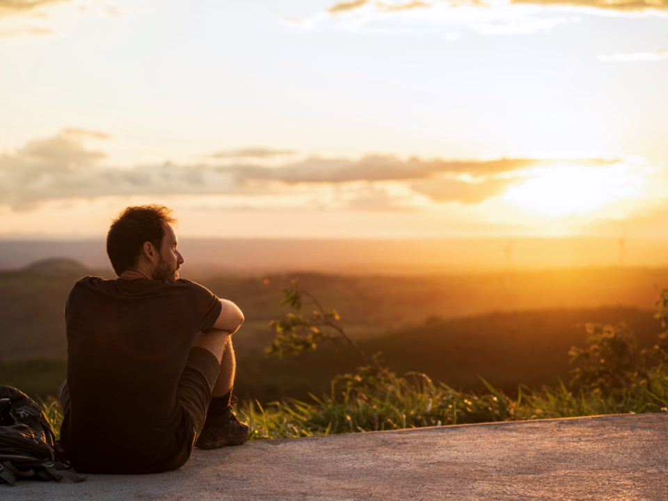 A photo of a man sitting down and looking at the sunset