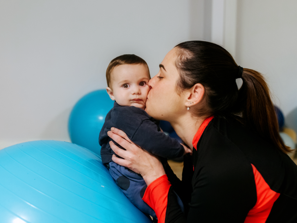 A woman kissing her baby who sits on an exercise ball