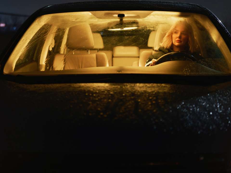 A woman sits alone in a car at night.