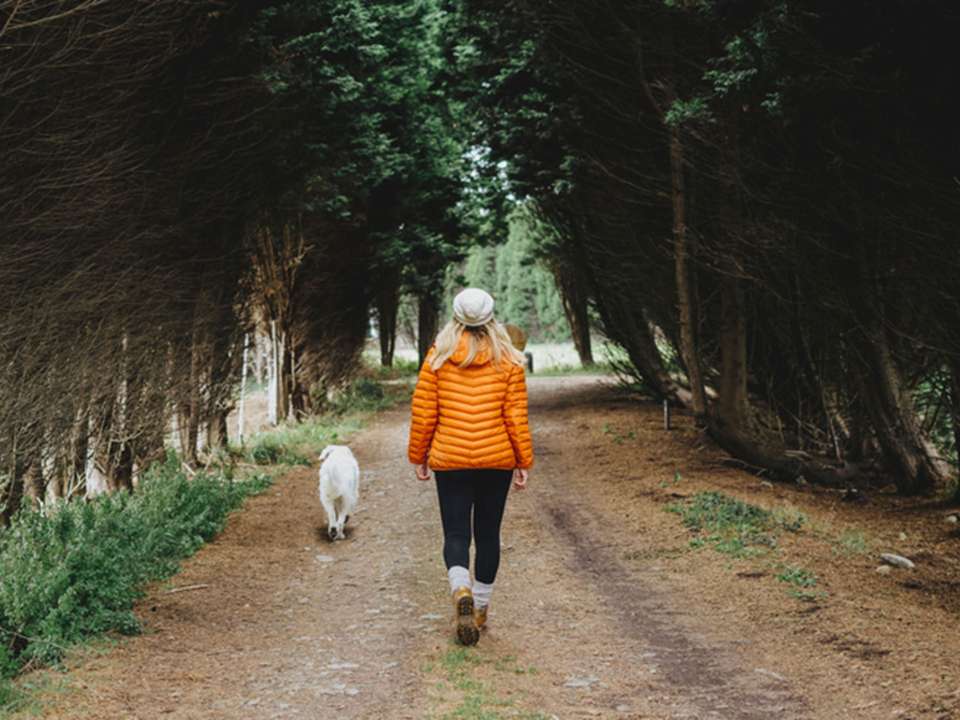 Woman in orange jacket walking her dog down a path