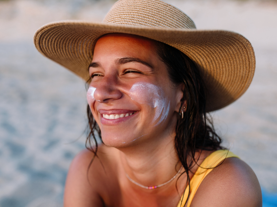 A woman sitting on the beach with sunscreen on her face