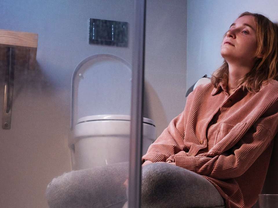 Woman sitting on bathroom floor next to toilet 