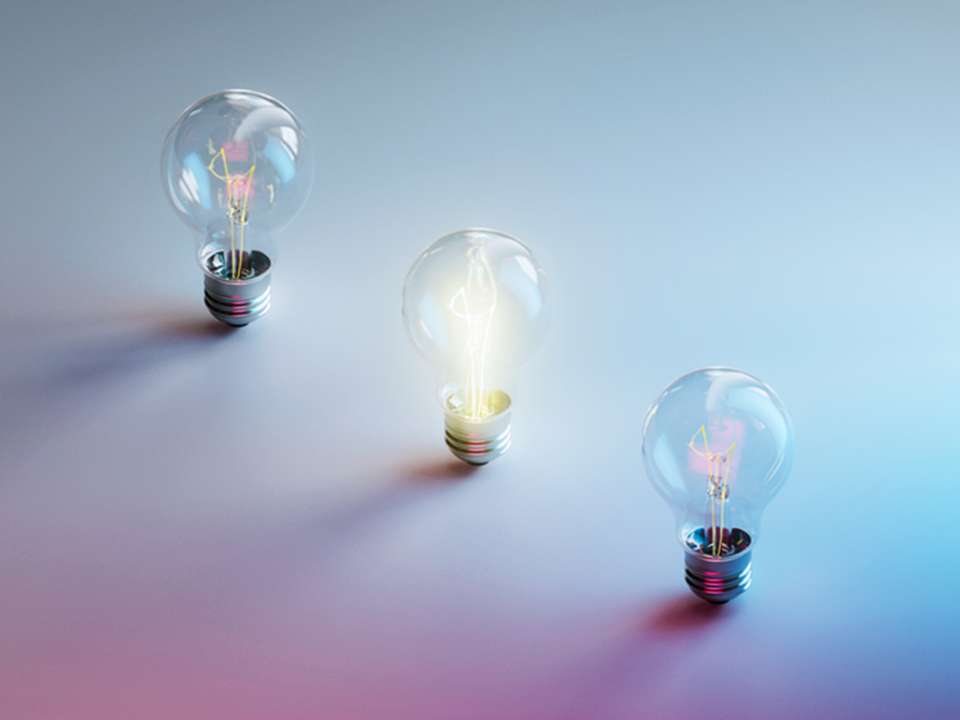 Three lightbulbs, one lit, on a hazy blue and pink background.