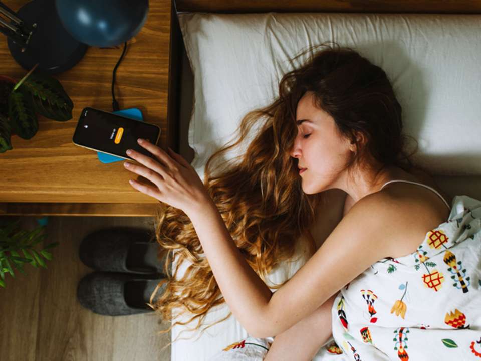 A woman lying in bed reaches for her phone alarm.